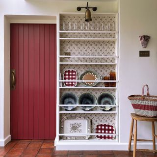 brass light over shelving with wallpaper back and red door and terracotta tiles
