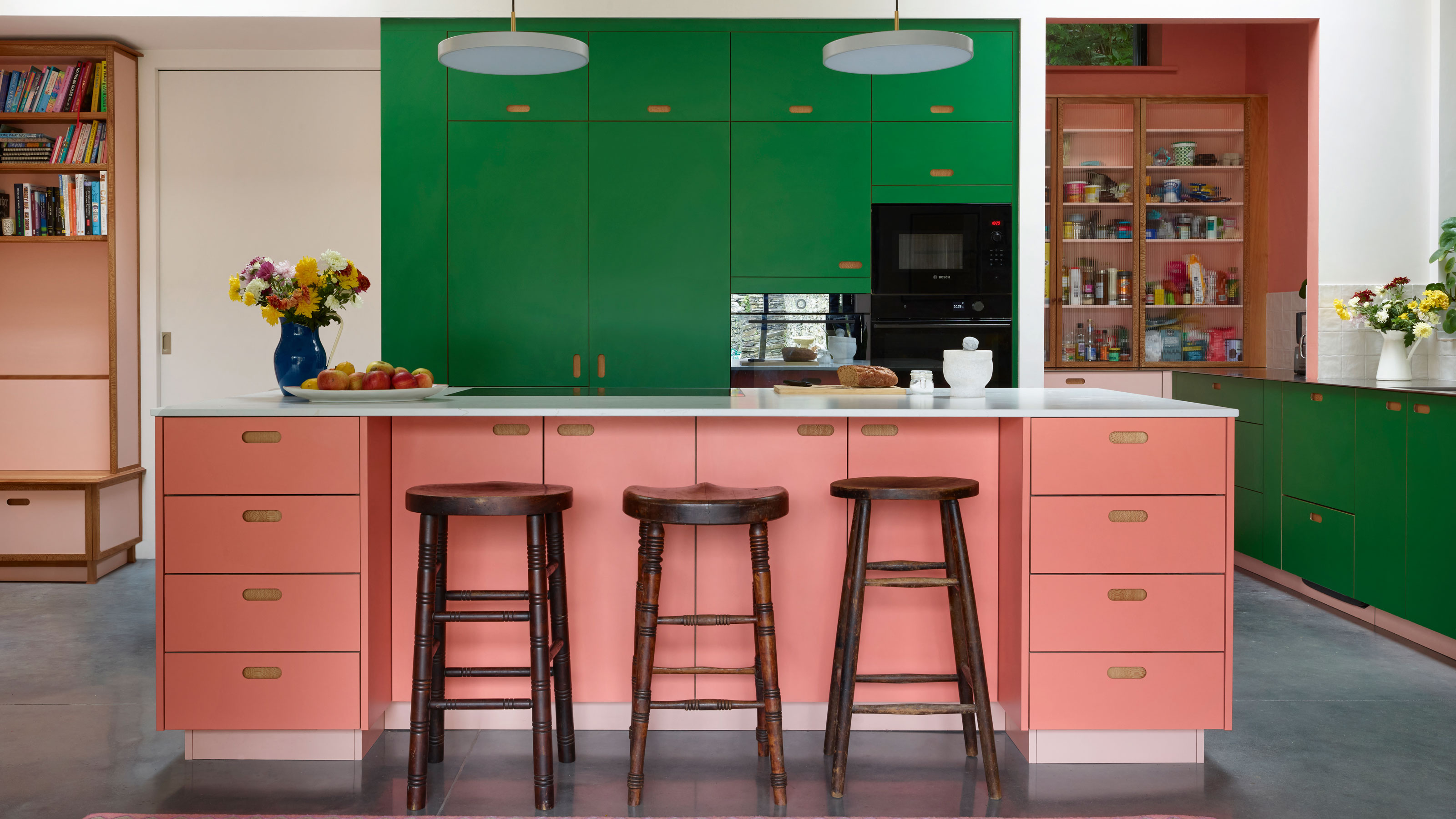 Pink and green kitchen with wooden bar stools and a blue rug