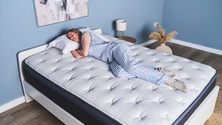 Woman wearing blue striped pajamas sleeping on a plush bed in a bedroom with a pastel blue wall