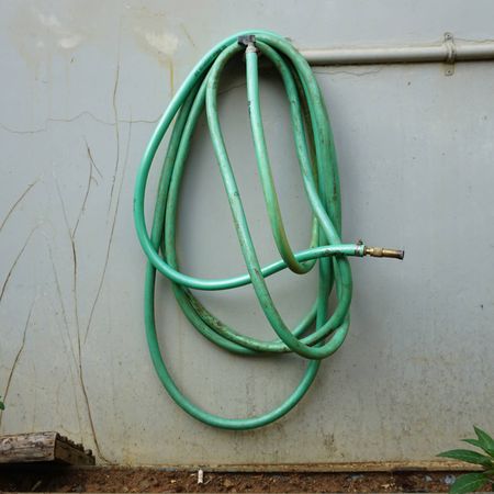 Old green garden hose hangs from tap on exterior wall