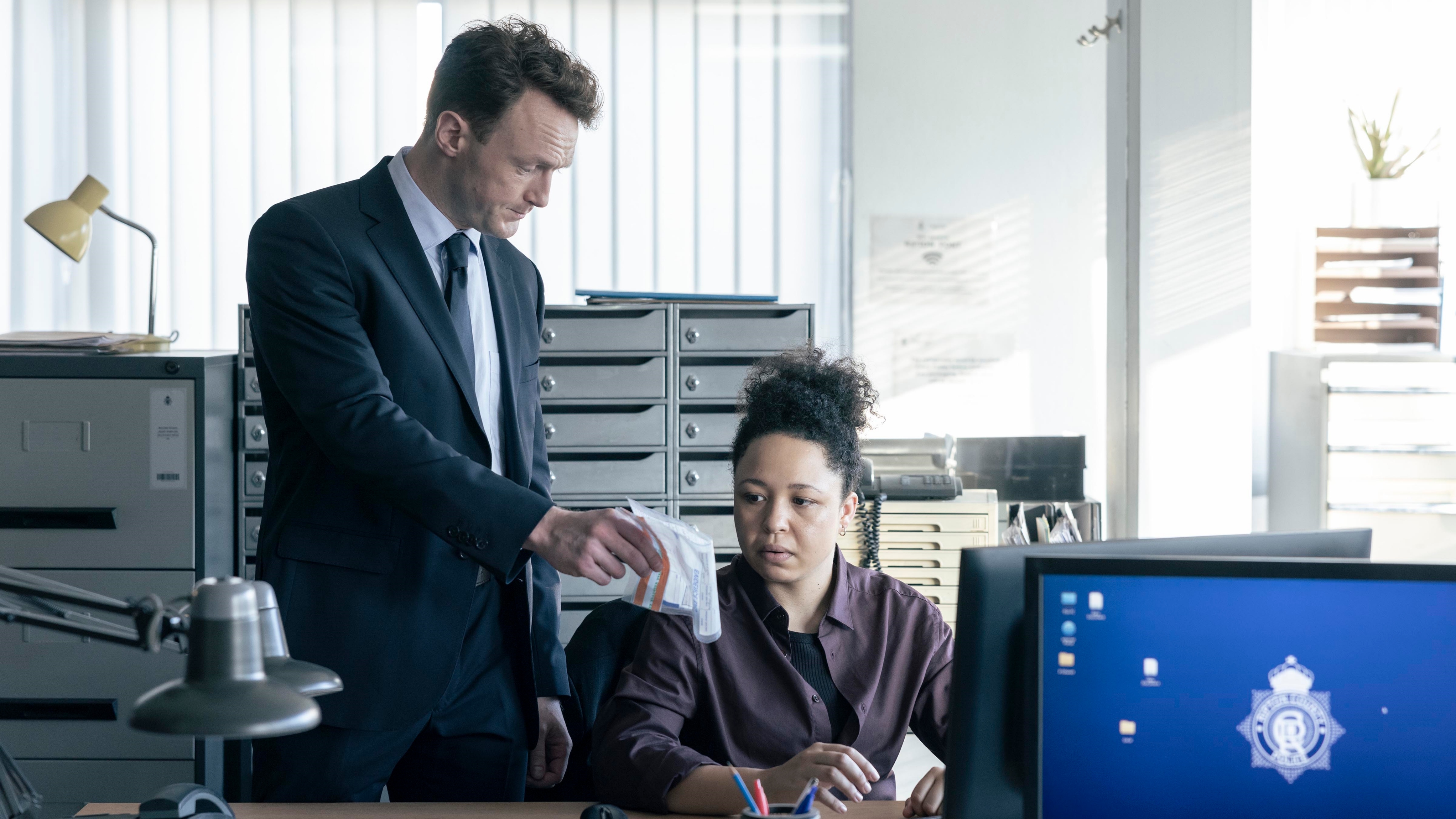 Jenny at work sitting at her desk at the police station looking at an evidence bag
