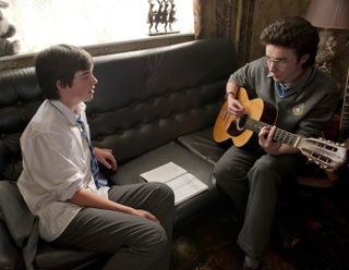 two teenage boys sing and play guitar sitting on the couch in the movie Sing Street