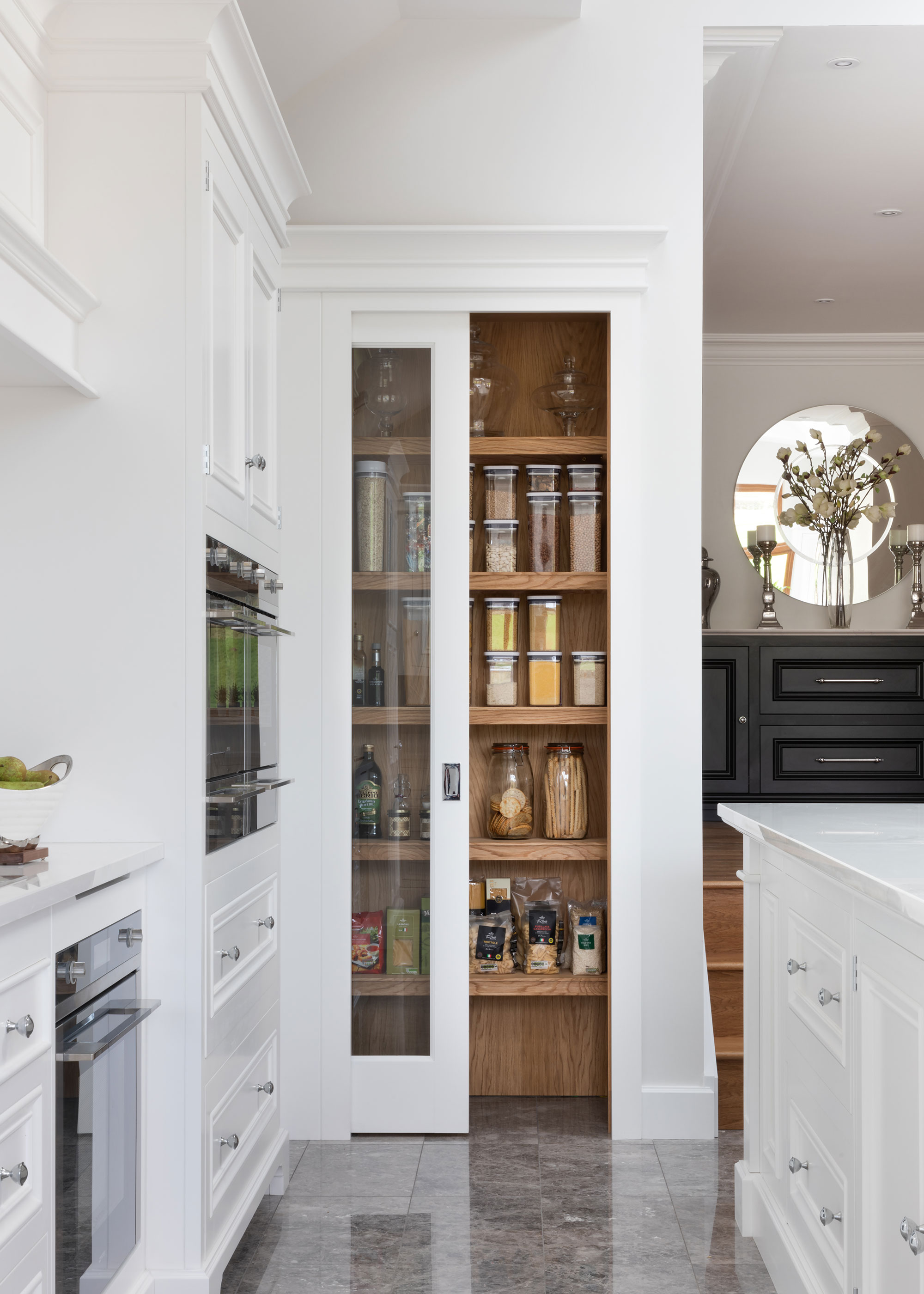 A small, pocket pantry in an all-white kitchen with sliding glass door. The shelves are lined with storage organizers.