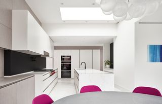 Large white kitchen with grey round table and pink chairs