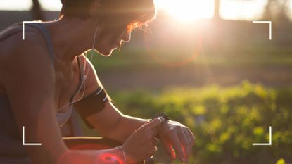 Woman checking fitness smartwatch, sitting down in the sunshine with headphones after running for weight loss