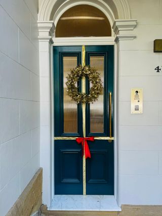 White house exterior with an emerald green front door. The door is wrapped in gold ribbon with a red bow and there is a gold wreath.