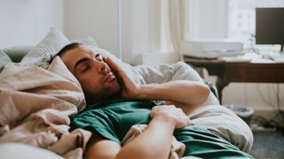 Man rubs his eyes as he has to wake up early despite not getting enough sleep