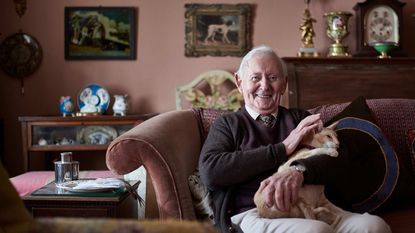 An older man sits in his living room filled with antiques.