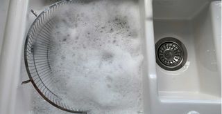 a white butler sink filled with soapy water to show how to clean a fan