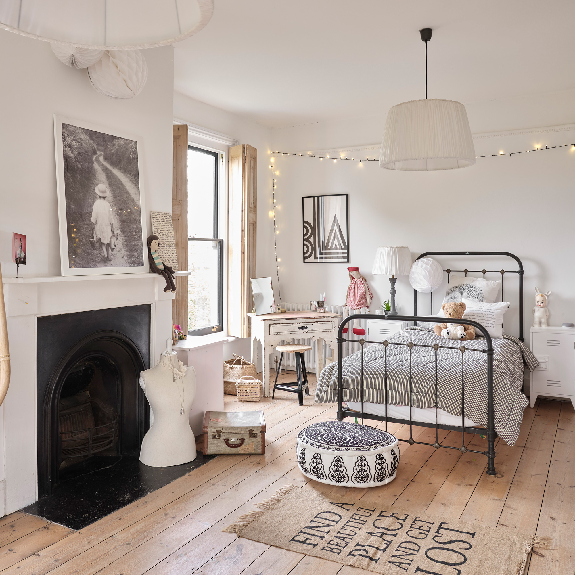 a child&#039;s bedroom with a wrought iron single bed, fireplace surround, neutral decor and fairy lights