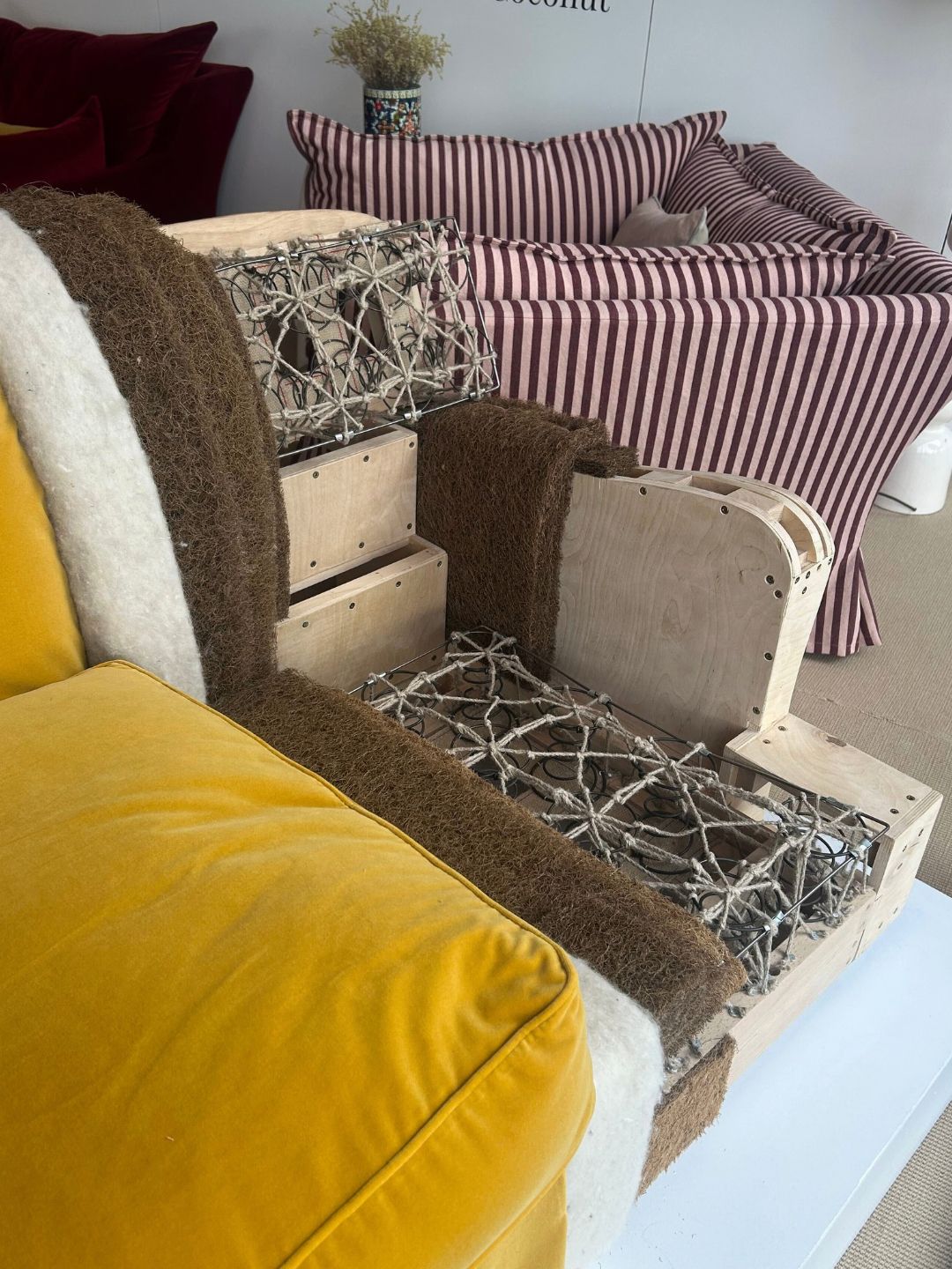Cutaway sofa at Schplendid's London showroom revealing eight-way hand-tied springs, a wooden frame, coconut fibre padding and layers of natural upholstery beneath a mustard velvet cushion.