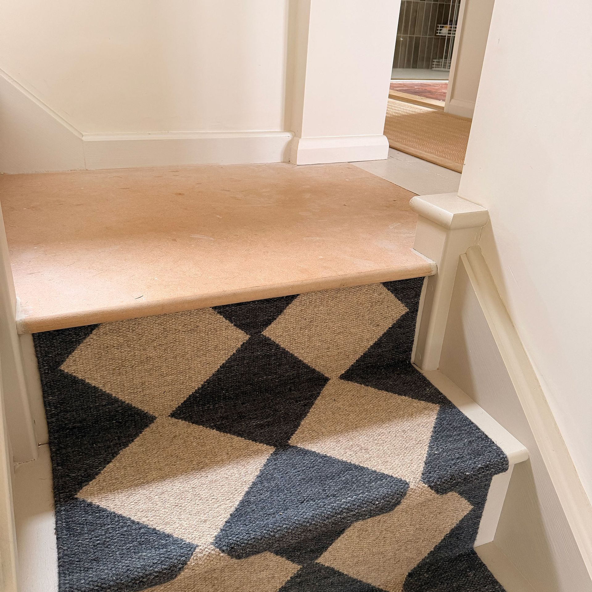 View up the stairs of black and neutral chequered runner, with plywood on landing