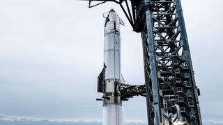 A silver spaceship atop the launch pad with gray clouds in background