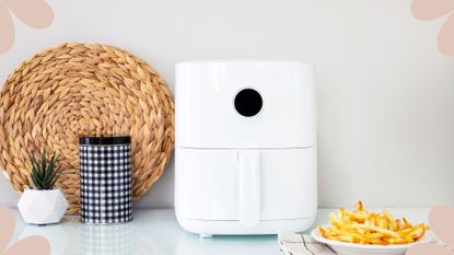 a white air fryer on a white kitchen countertop, with a kitchen behind and a bowl of homemade fries, to illustrate the question are air fryers healthy?