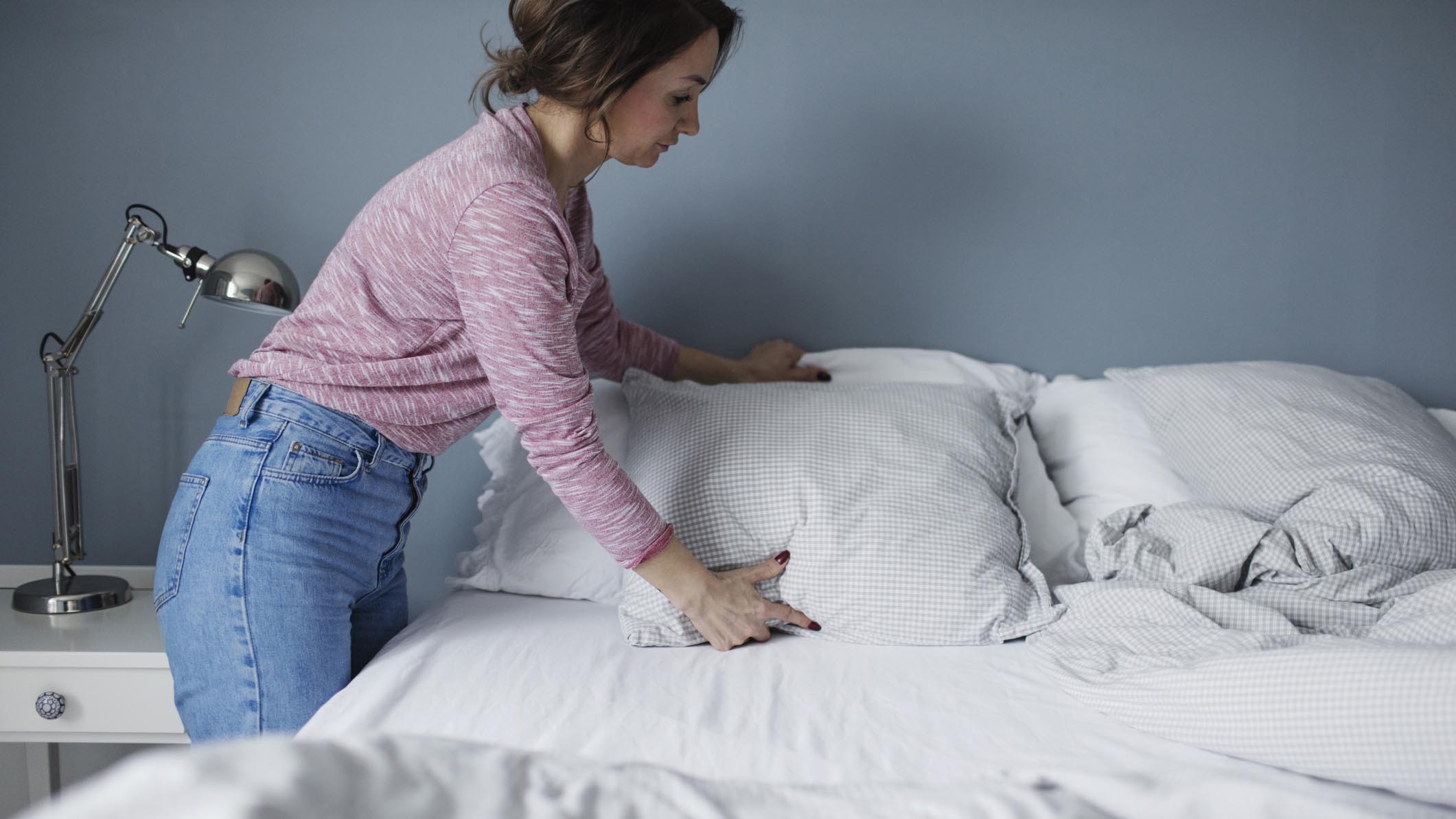 A woman plumps a freshly washed pillow before placing it on her bed