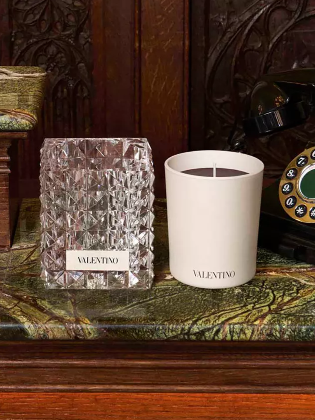 A ceramic Valentino candle beside a crystal holder on a green marble side table
