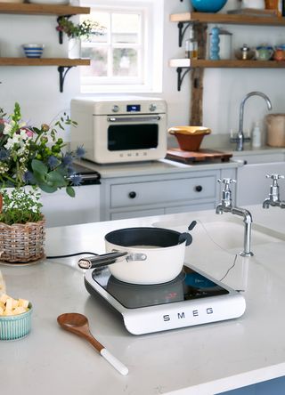 A white country kitchen with the new Smeg poratable induction hob on the kitchen island with a white pan cooking on top