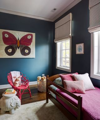 kids bedroom with dark teal walls, pink bedding and red chair with butterfly artwork on wall