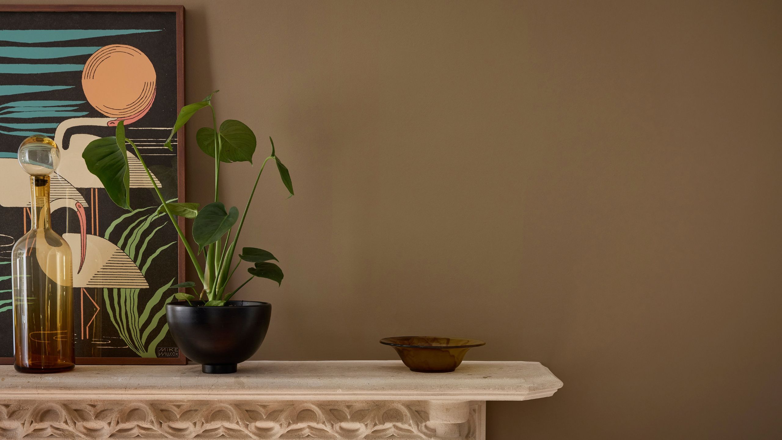 An up-close shot of a mantelpiece with a potted plant, a glass bottle, and a small dish on top, and a graphic print of swans behind, against a backdrop of Marle by Little Greene.