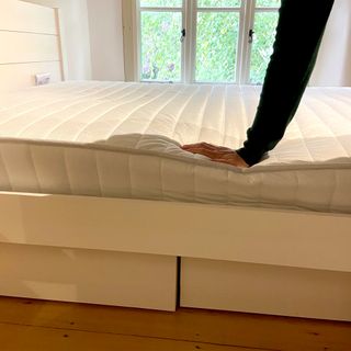 A womans hand pressing down on the edge of the Dreams Workshop Follows Traditional Spring Mattress