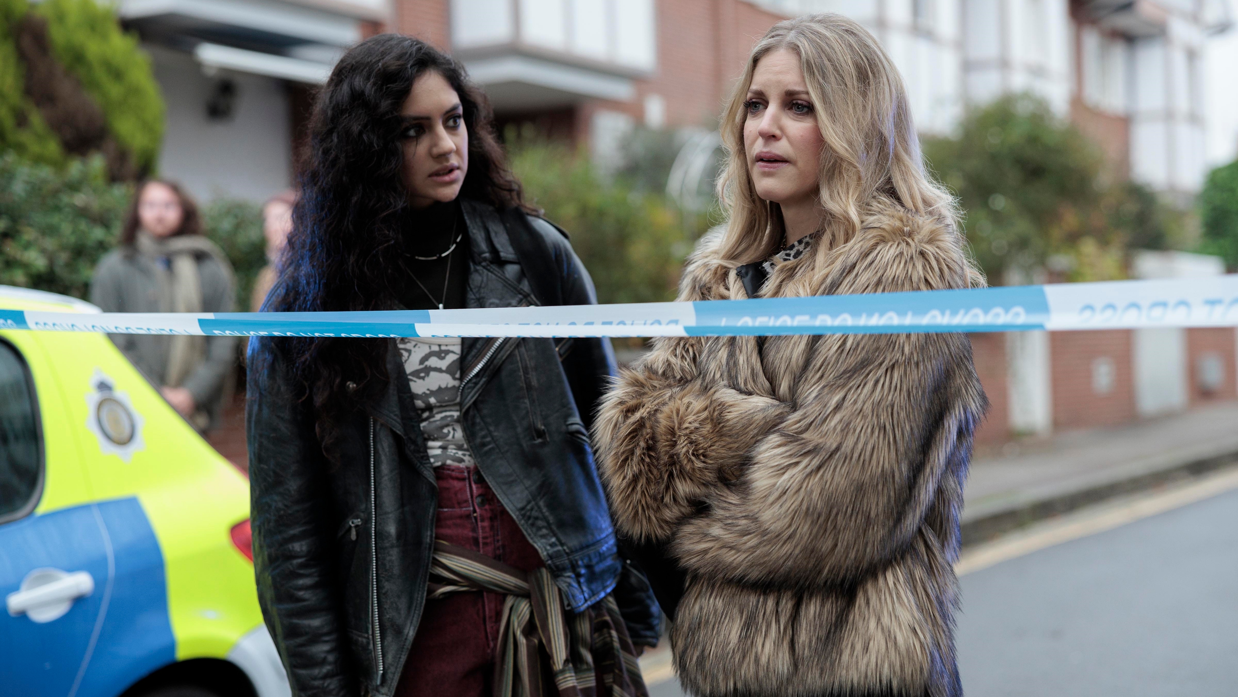 Liz and Margot argue in the street while standing behind a police crime scene barrier and next to a police car