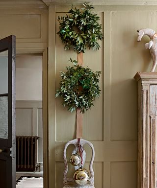 Two green wreaths hanging on neutral wall with ribbon
