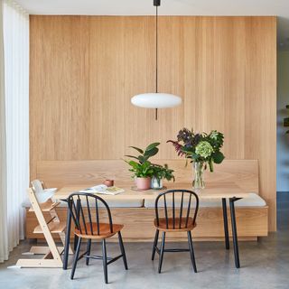 a dining area with wooden topped dining table, black dining chairs and a Stokke highchair and vertical wall panelling