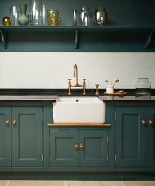 Forest green kitchen cabinets with white sink, brass faucet, black counter