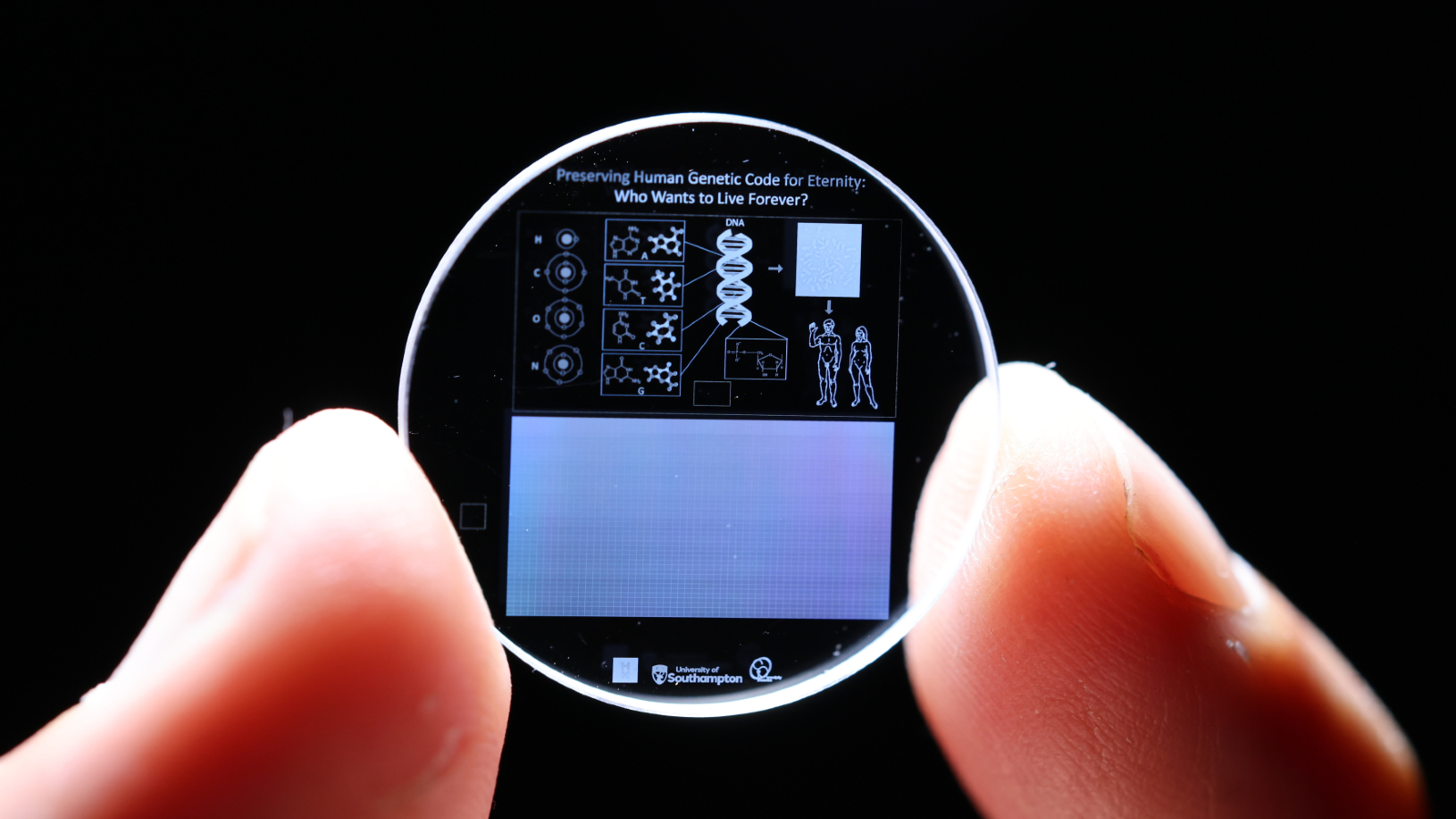 Un pequeño chip circular se sostiene entre las puntas de dos dedos humanos. Está cubierto por diagramas biológicos.