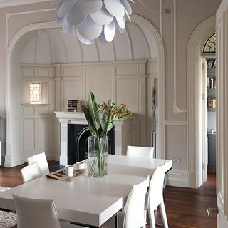 dinning room with cream colour wall white dinning table and white chair flower pot and wooden flooring