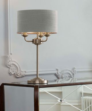 brass 3 light lamp on a glass side table with wall cornicing and moldings - Laura-Ashley