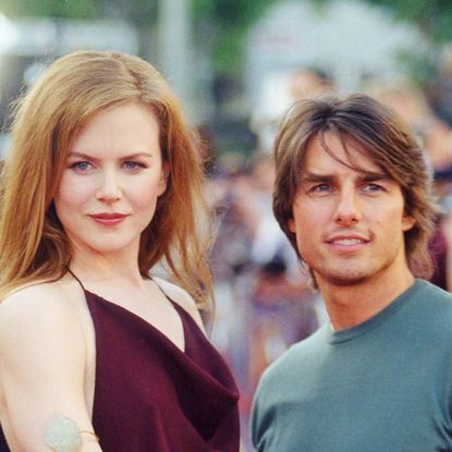 Nicole Kidman wears a strappy red top and long ginger hair as she poses with her then-husband Tom Cruise who wears a blue sweater