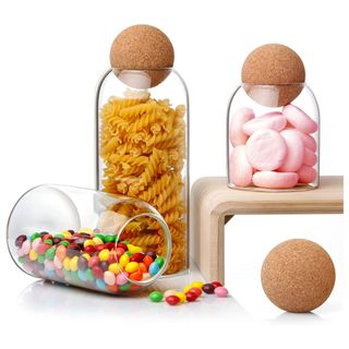 Three glass jars with cork ball lids are filled with pasta and candy