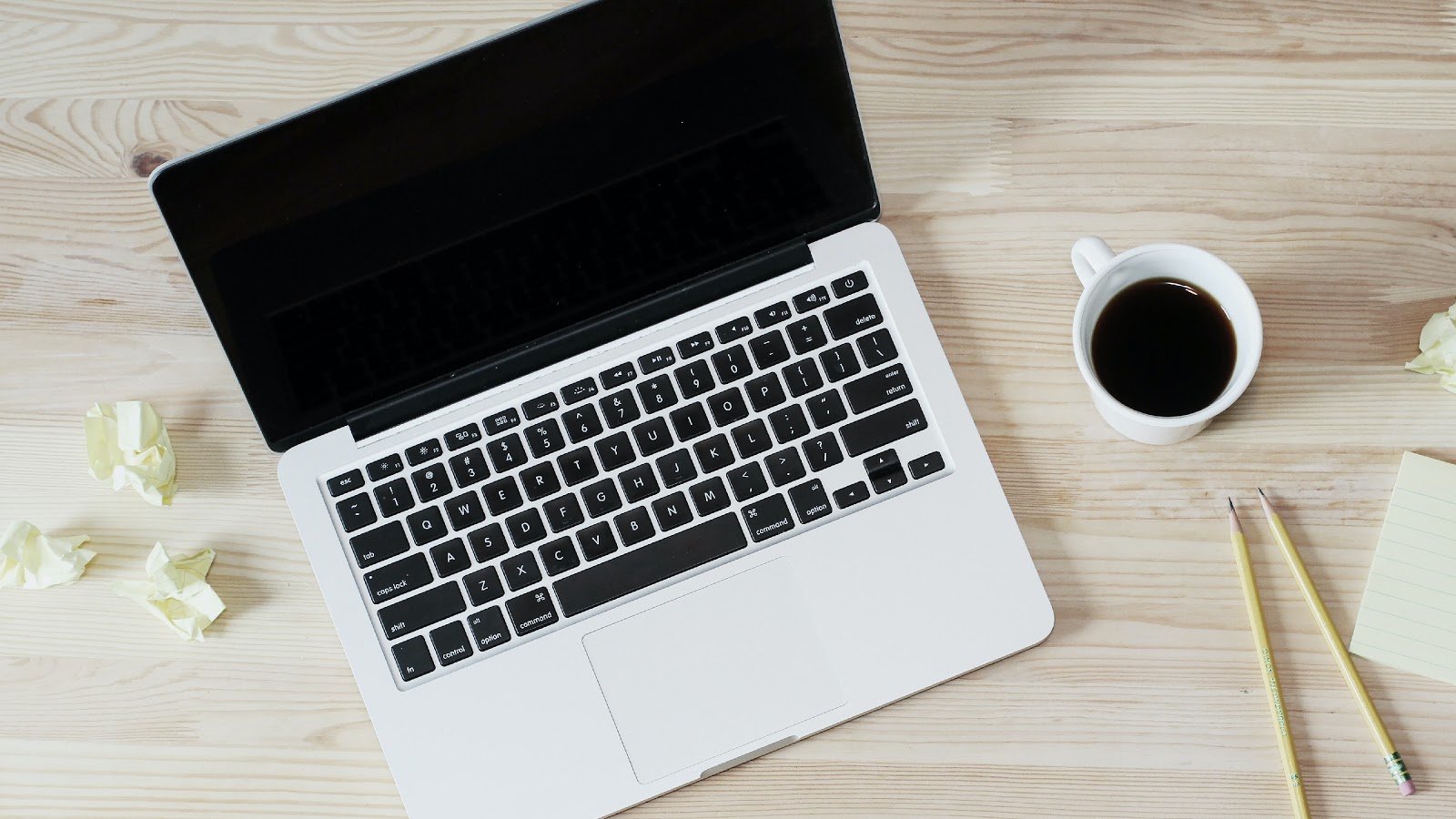 laptop, crumpled post-its, a mug of coffee and pencils on a table