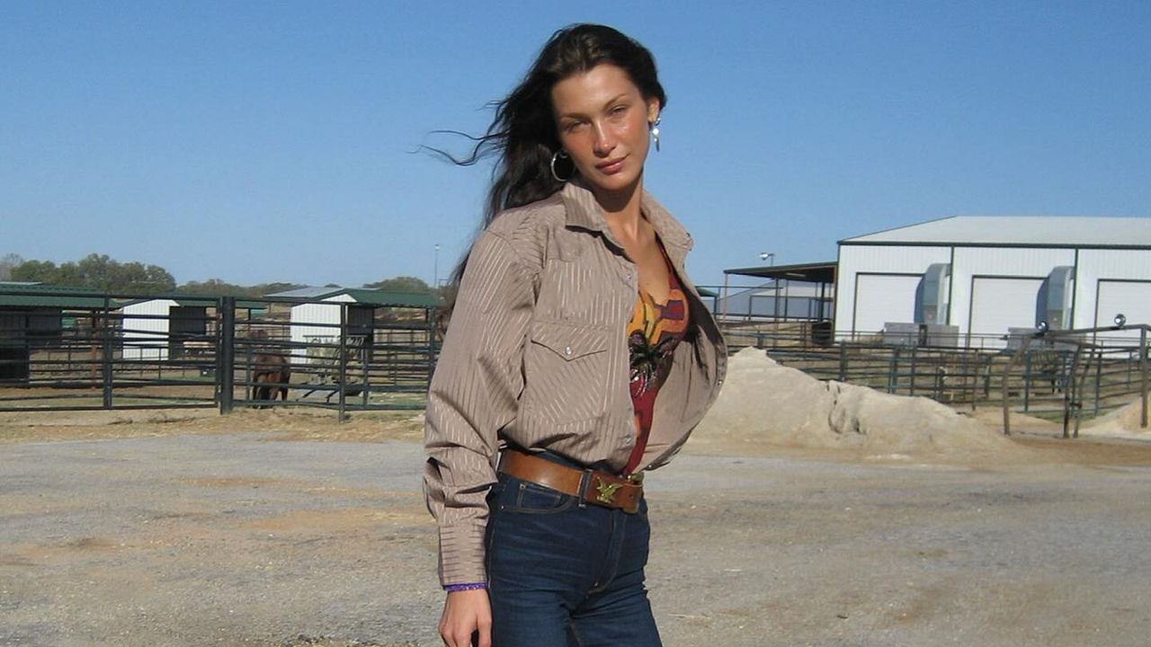 Bella Hadid wearing an open button down with a tank top and blue jeans with a brown belt