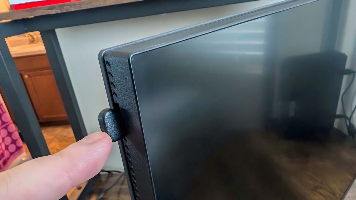 A finger pressing the button on the top left side of the Alienware AW2725QF Gaming Monitor.