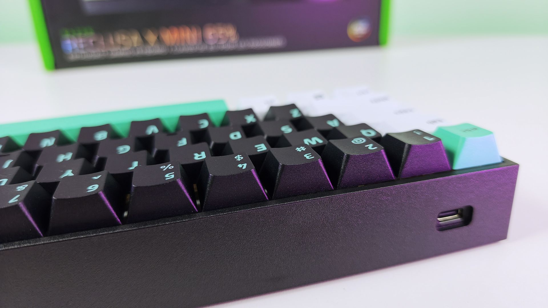 Close-up side view of the Razer Reclusa X Mini 65% keyboard showing the recessed USB-C port on its black frame.