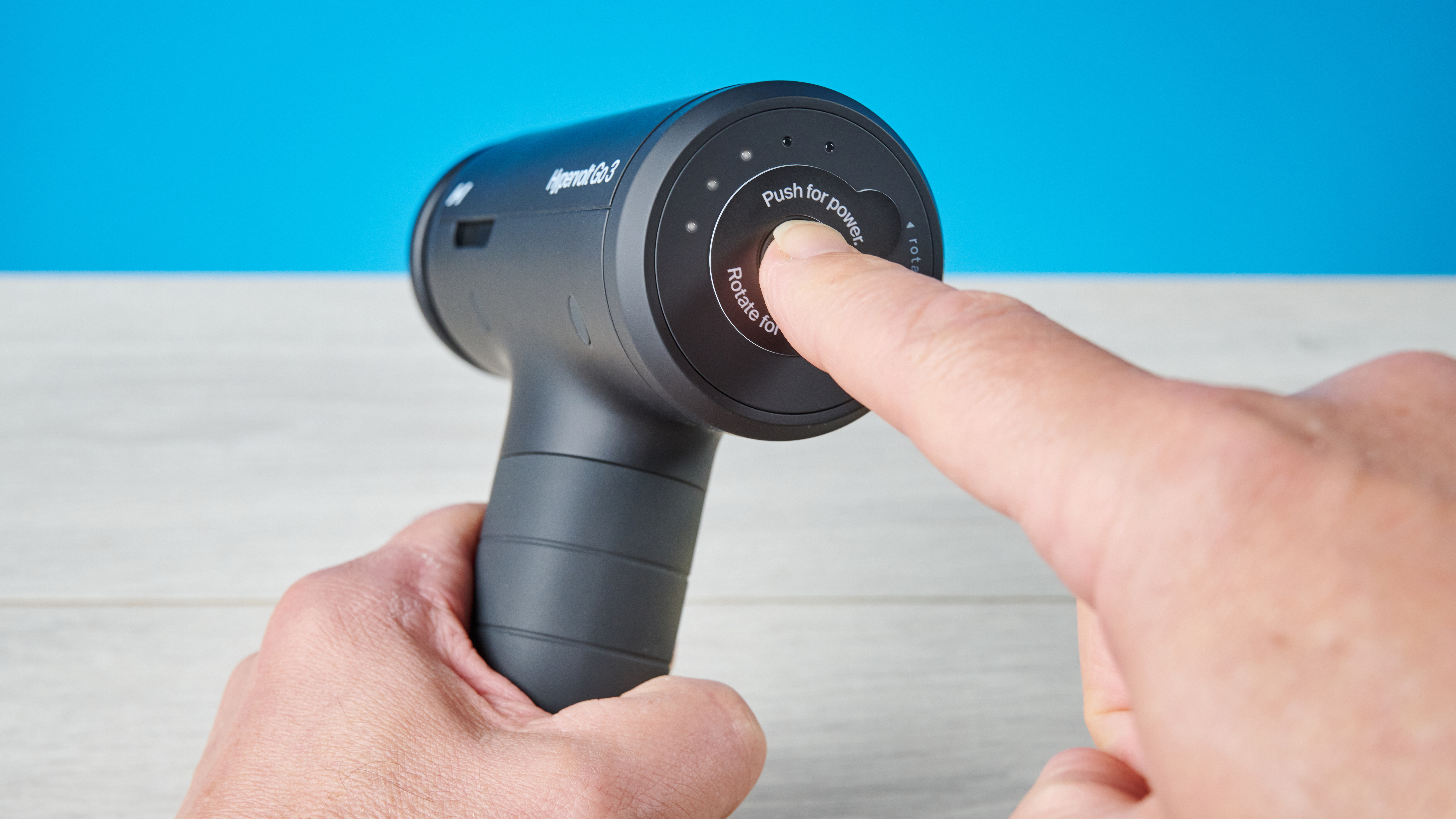 Hyperice Hypervolt Go 3 massage gun photographed in front of a blue background