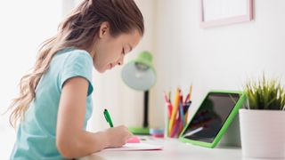 happy girl with tablet pc computer writing to notebook at home