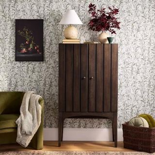 A wooden paneled cabinet in front of green and white floral wallpaper