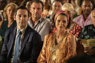Death in Paradise Christmas special 2022 Neville (Ralf Little) and Catherine (Élizabeth Bourgine) sit in church for a Christmas carol service, surrounded by fellow residents