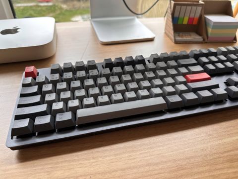A Space Grey Wombat Pine Pro keyboard sitting on a brown wooden desk
