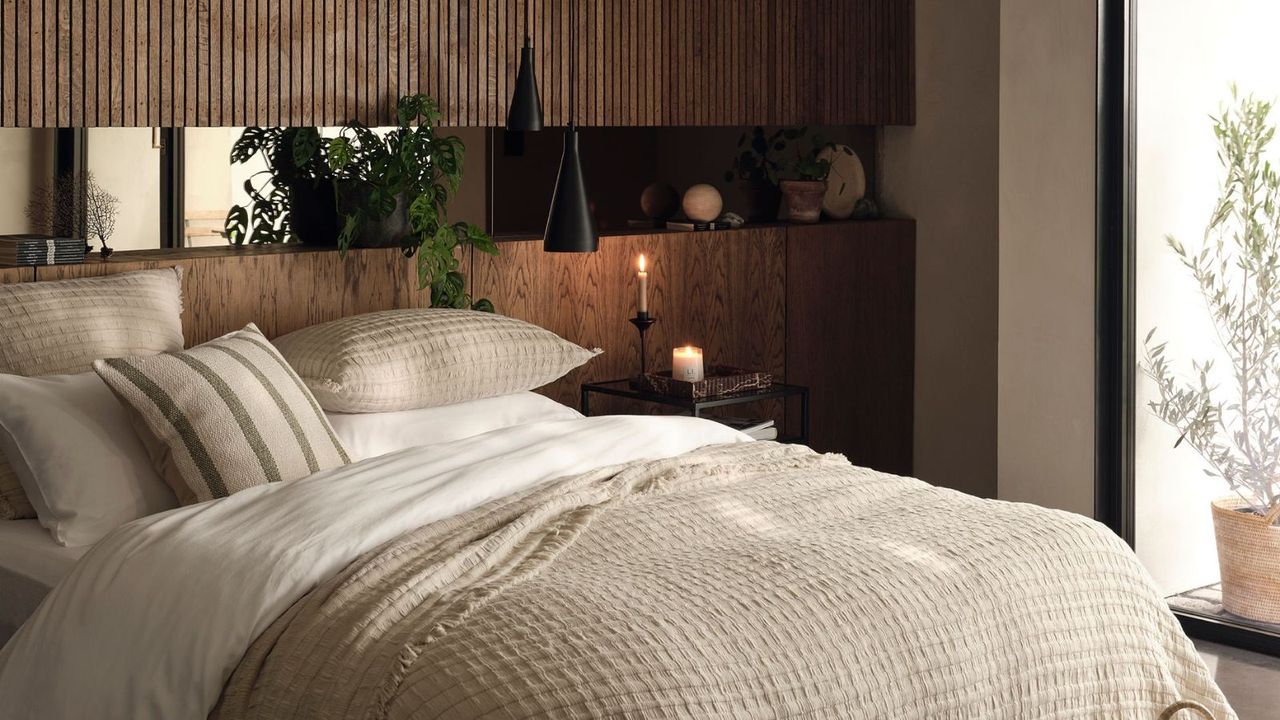 A warm rustic bedroom with wooden headboard stretching aling a whole wall, and a large bed with neutral bedding