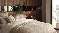 A warm rustic bedroom with wooden headboard stretching aling a whole wall, and a large bed with neutral bedding