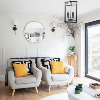 living room with grey sofa and designed cushion white wall round mirror and wooden flooring