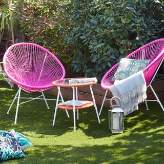 tropical garden with green plants and grass lawn with pink chairs and table