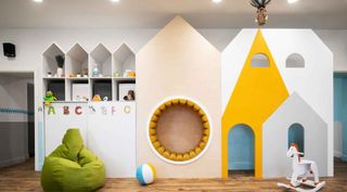A kids playroom with a castle shaped play house, a green been bag and a rocking horse.