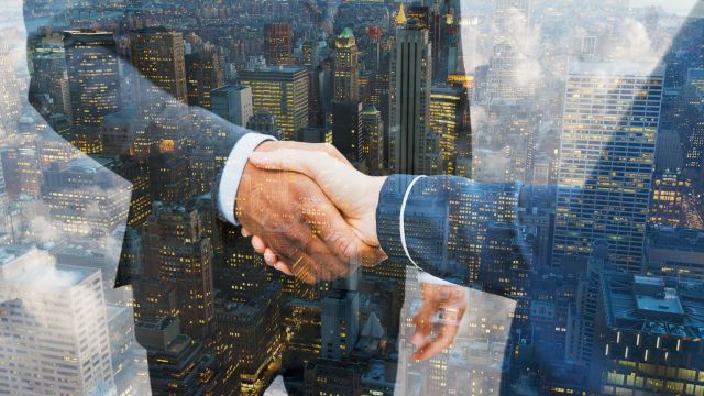 Two men shaking hands with a cityscape superimposed. 