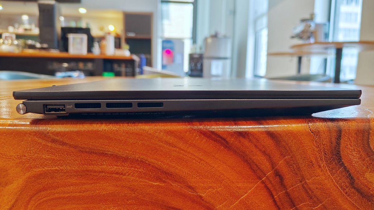 Asus Zenbook 14 OLED UM3402Y closed on a wooden desk showing the ports on its left side.