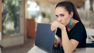 Young woman turns laptop away from camera while looking at camera suspiciously.